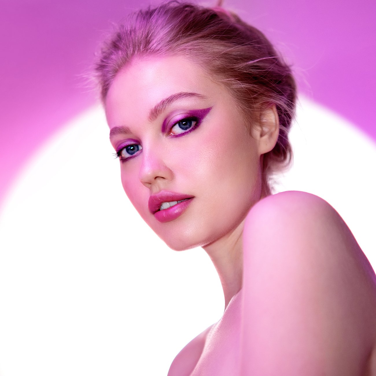 Dziewczyna w fioletowym makijażu oczu, w neonowym świetle na różowym tle