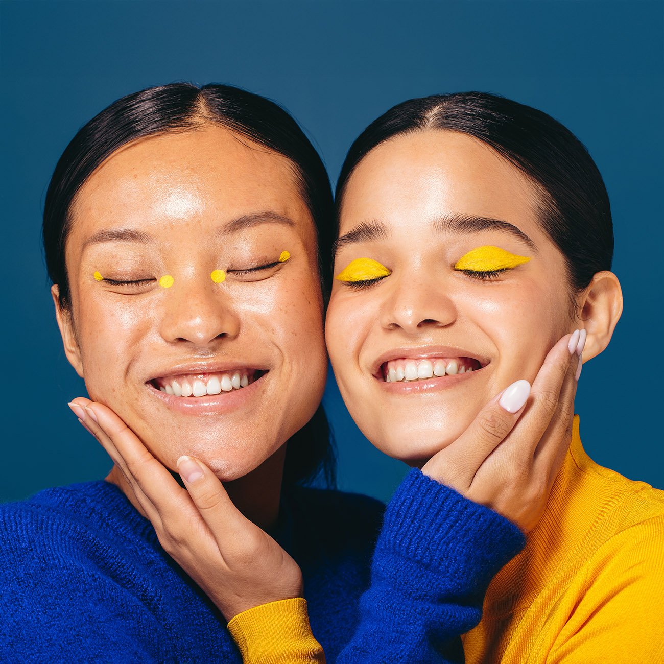 Dwie uśmiechnięte młode kobiety w żółtym i niebieskim makijażu, obejmujące się
