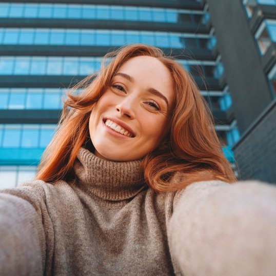 Rudowłosa kobieta w makijażu robi selfie na tle biurowca