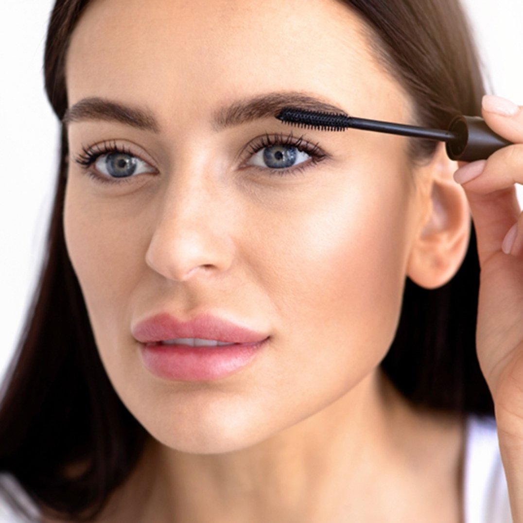 Portret kobiety w delikatnym makeupie malującej przed lustrem rzęsy tuszem