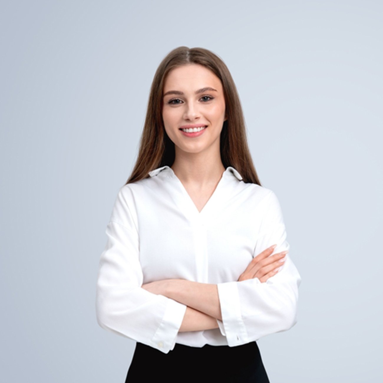 Uśmiechnięta młoda kobieta w białej koszuli stojąca z założonymi rękami na szarym tle