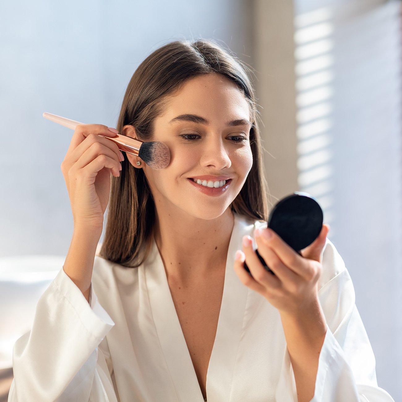 Uśmiechnięta młoda kobieta wykonująca w łazience dzienny makijaż