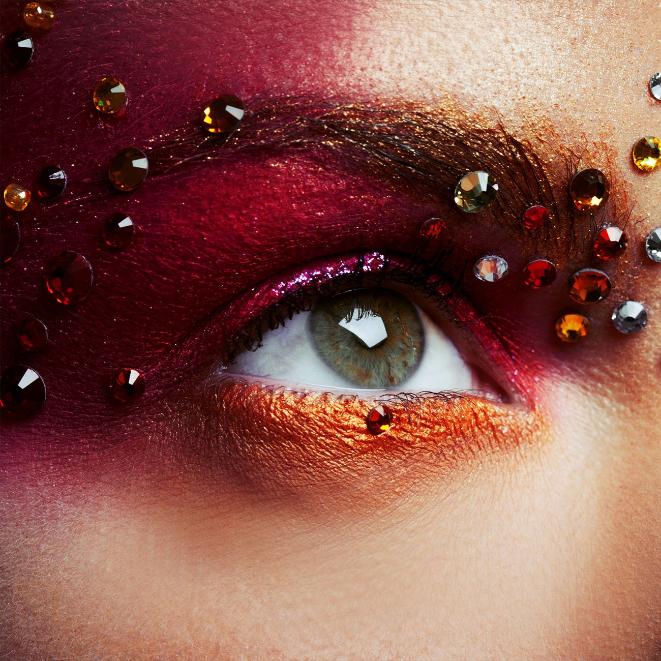 Zbliżenie na oko pokryte czerwonym i pomarańczowym cieniem oraz kryształkami