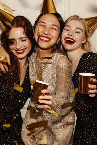 Przyjaciółki w makijażu na imprezę bawią się i trzymają złote kubki