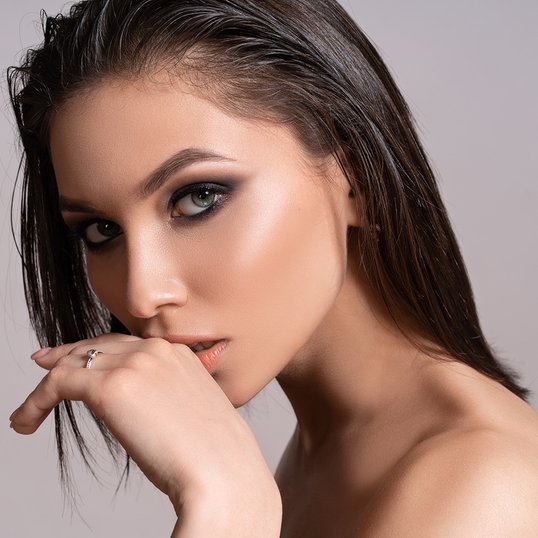 Ciemnowłosa kobieta na jasnym tle z profesjonalnie wykonanym smokey eyes
