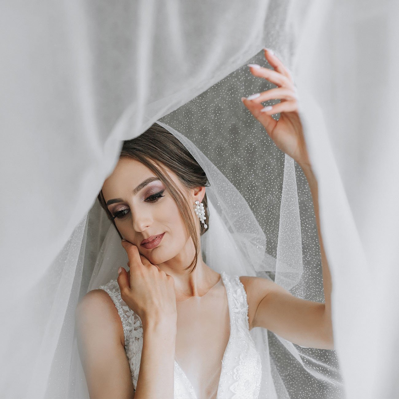 Panna młoda dotyka twarzy, ujęcie pod przezroczystą tkaniną