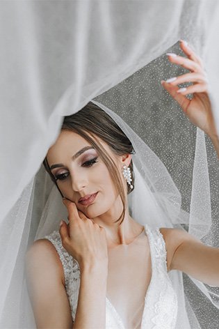 Panna młoda dotyka twarzy, ujęcie pod przezroczystą tkaniną