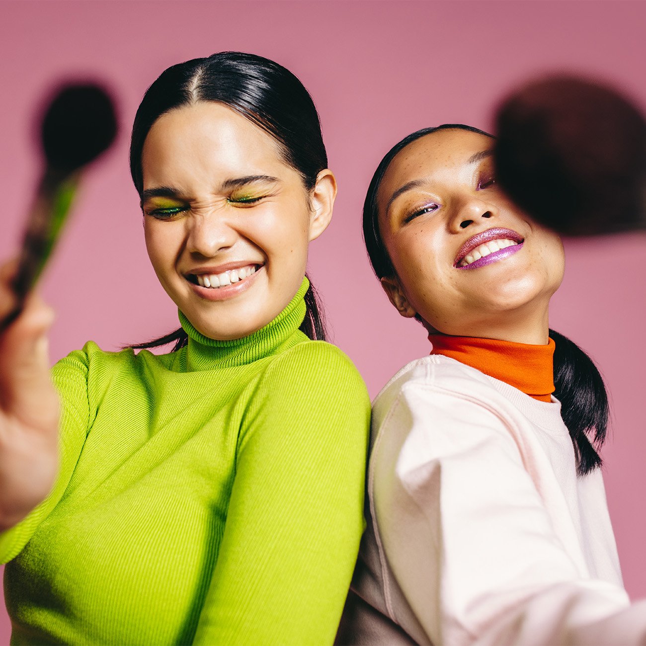 Młode uśmiechnięte kobiety z kolorowym makijażem zbliżają pędzle do obiektywu