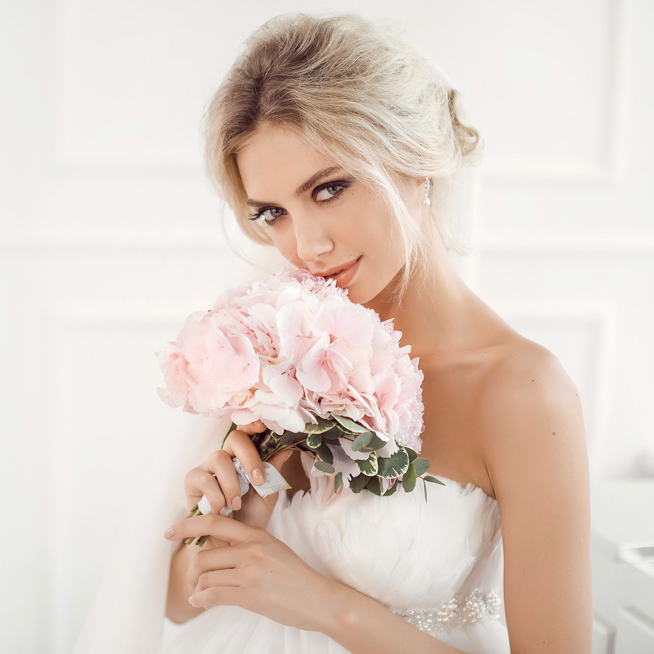 Kobieta z długimi włosami w kolorze blond w sukni ślubnej i makijażu ślubnym trzyma bukiet różowych kwiatów