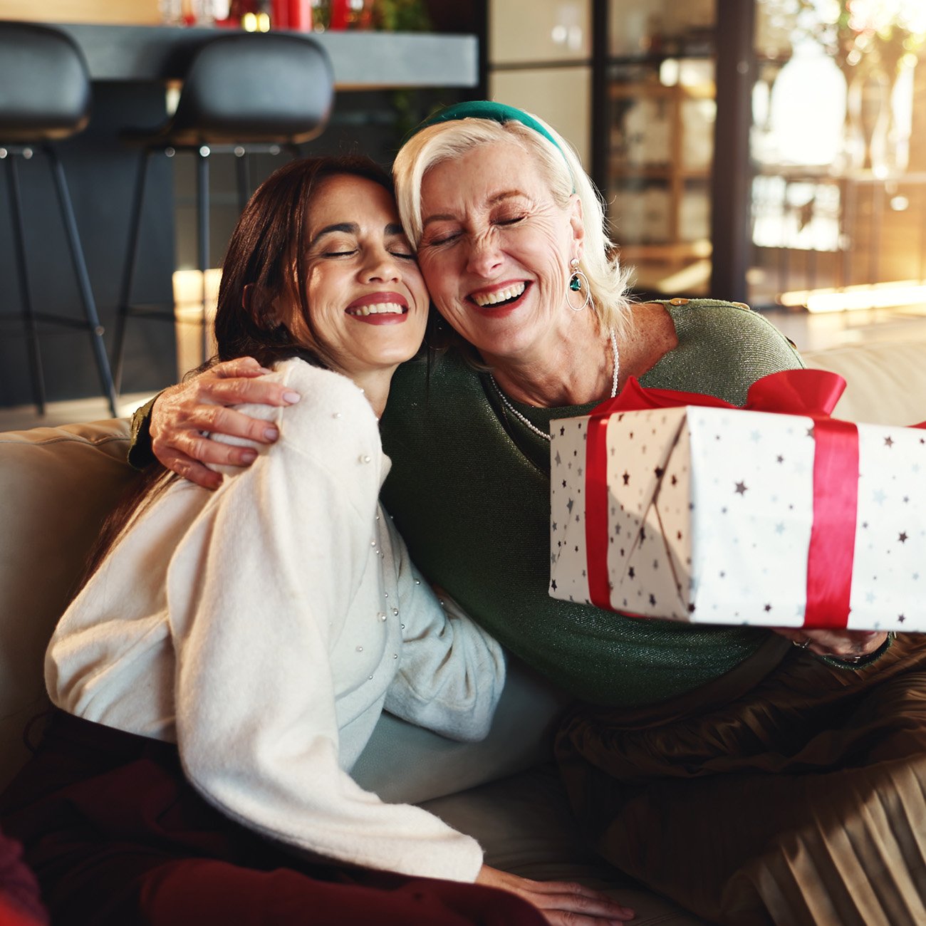 Dwie kobiety przytulające się na kanapie, jedna ze świątecznym prezentem w ręku
