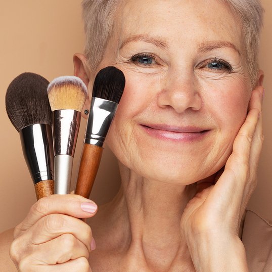 Dojrzała kobieta w makeupie trzymająca w dłoni pędzle do makijażu