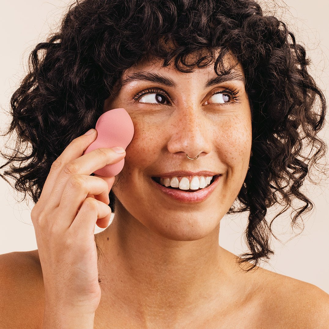 Kobieta w kręconych włosach przykłada do twarzy gąbeczke beauty belnder