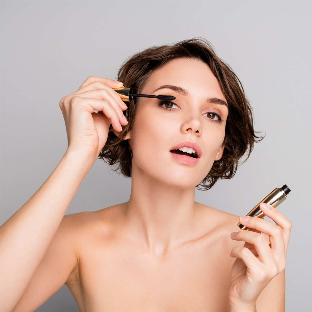 Krótkowłosa kobieta na jasnym tle maluje rzęsy.