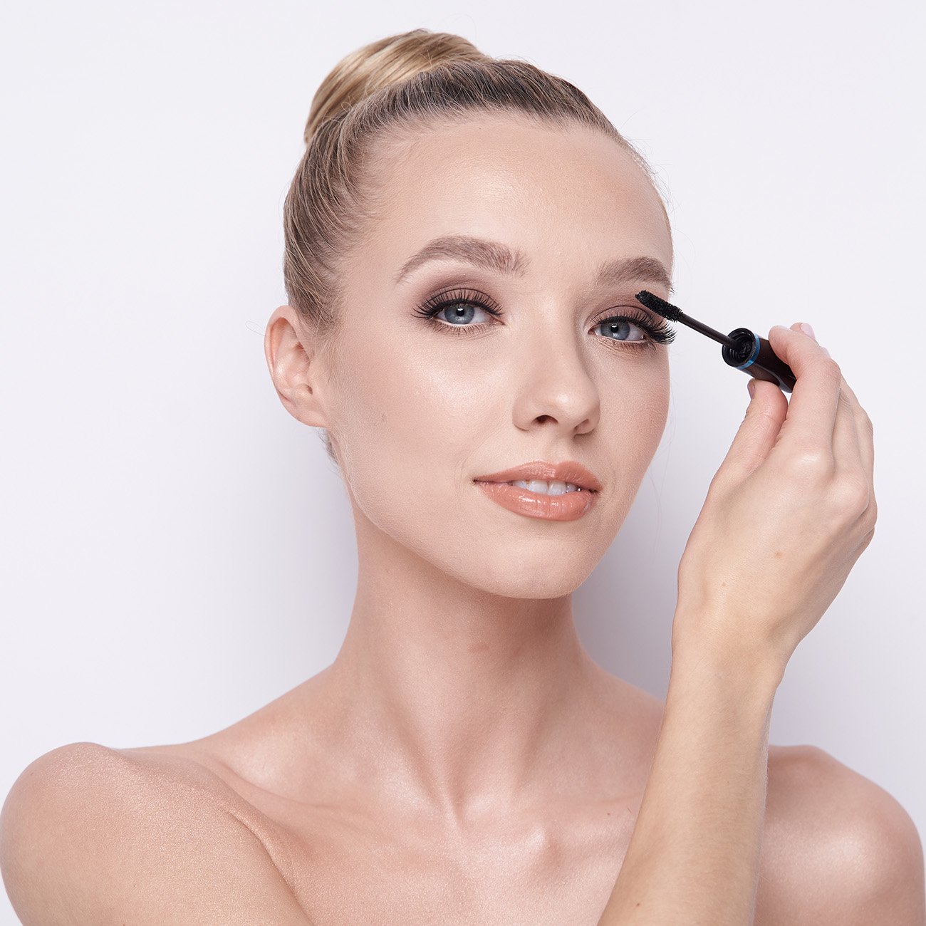  Blondwłosa kobieta na białym tle w naturalnym makijażu wykonuje makijaż rzęs.