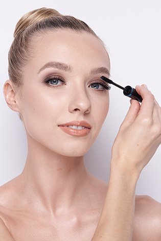 Blondwłosa kobieta na białym tle w naturalnym makijażu wykonuje makijaż rzęs.