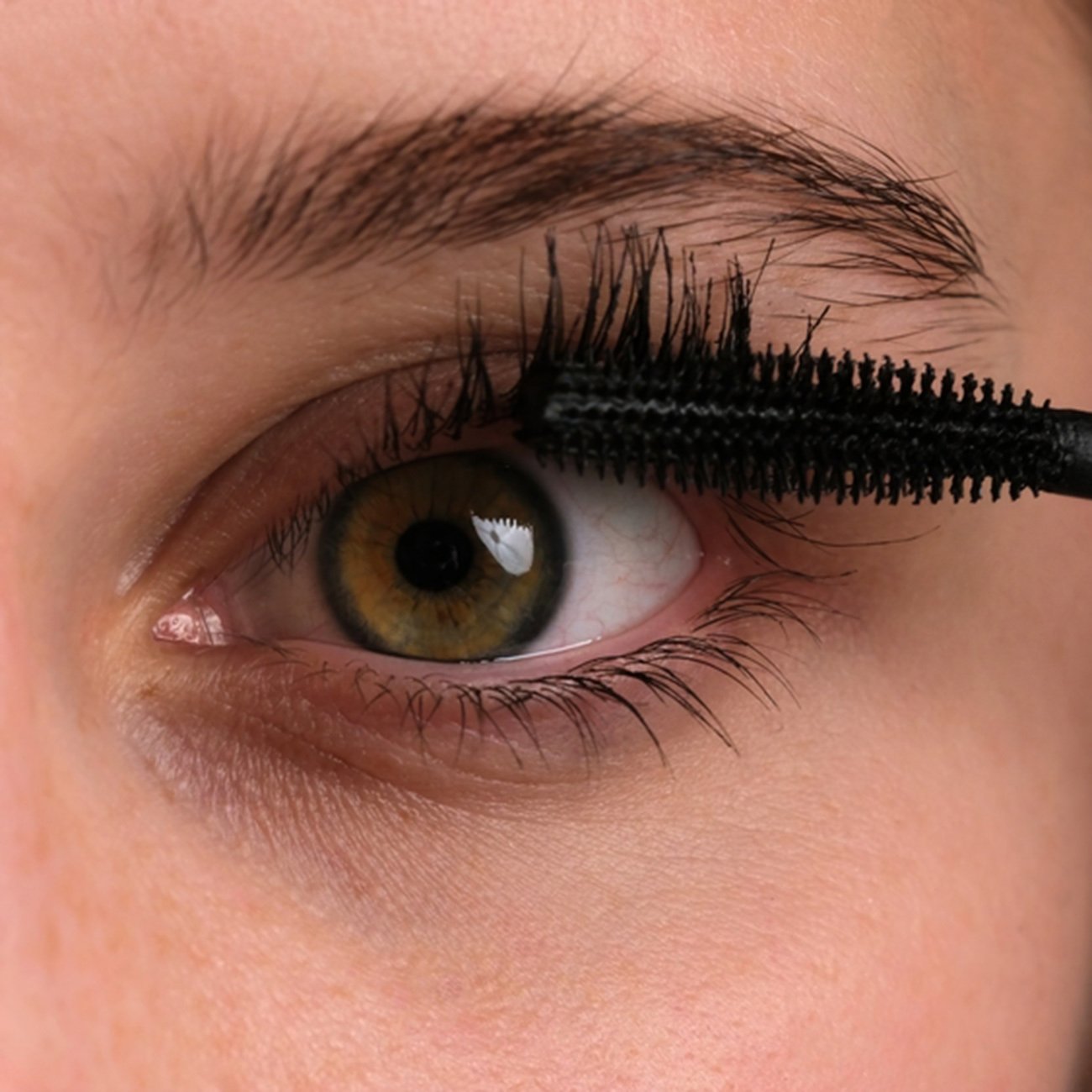 Zbliżenie na kobiece oko w czasie malowania rzęs maskarą