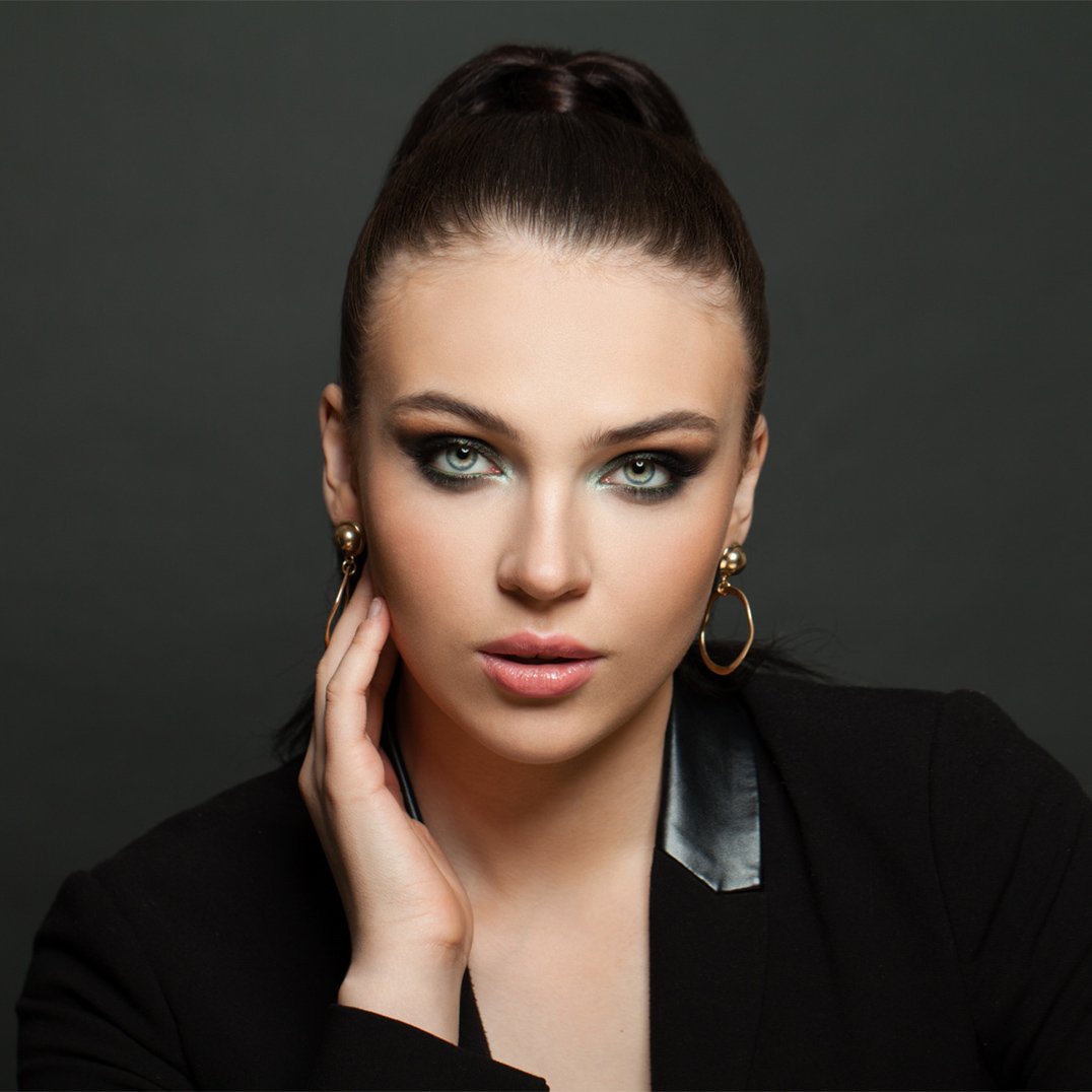 Piękna kobieta na ciemnym tle z makijażem smokey eyes w odcieniach zieleni.