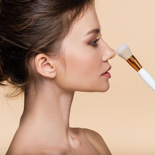 Portret z boku brunetki trzymającej przed twarzą pędzel do make upu