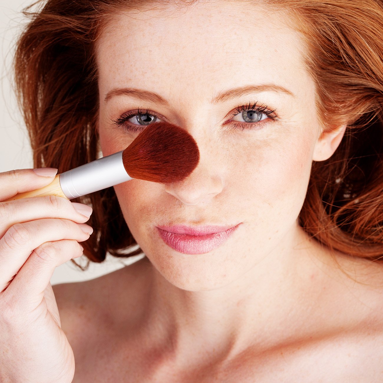 Ruda kobieta konturująca sobie nos pędzlem do makijażu