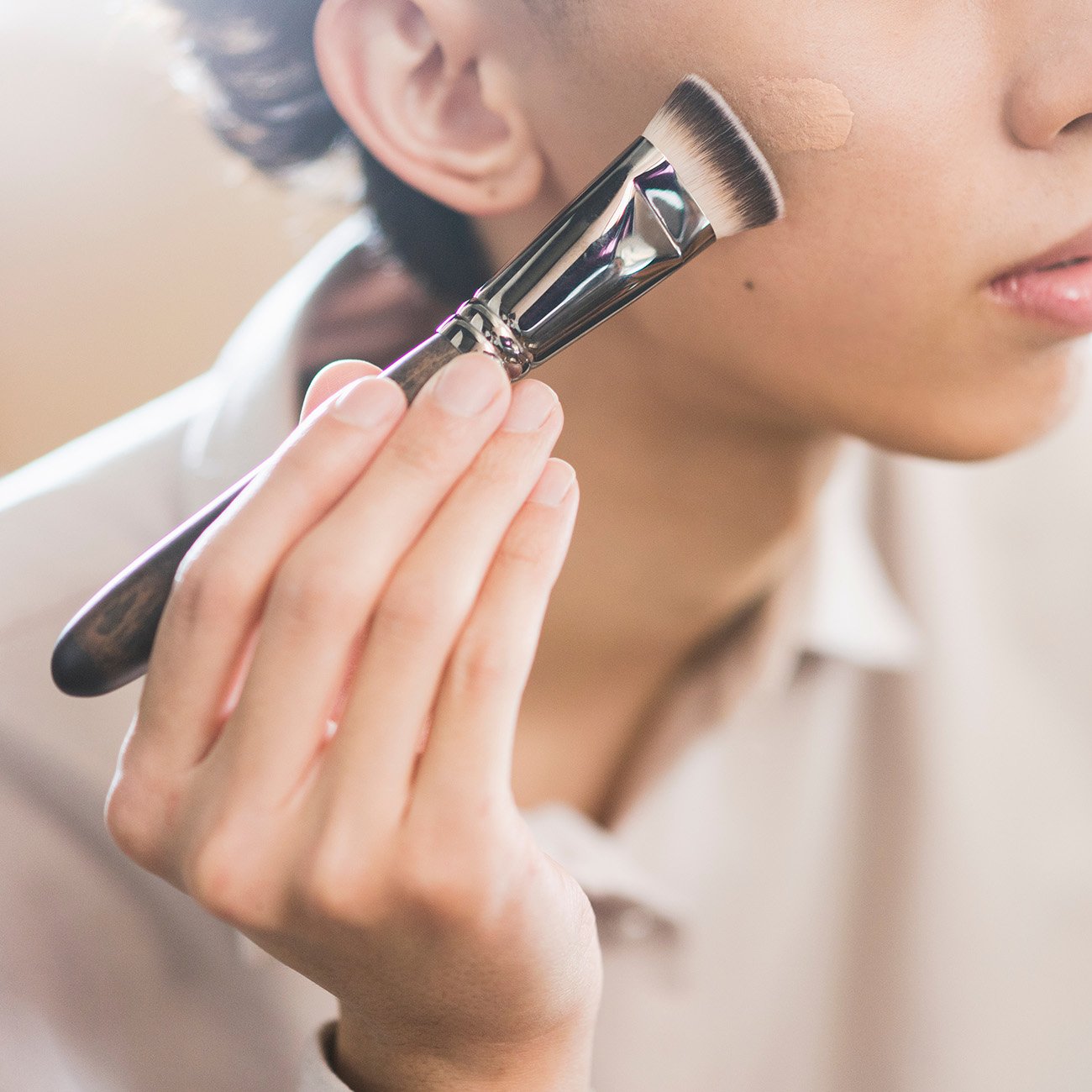 Kobieta nakłada podkład za pomocą pędzelka.