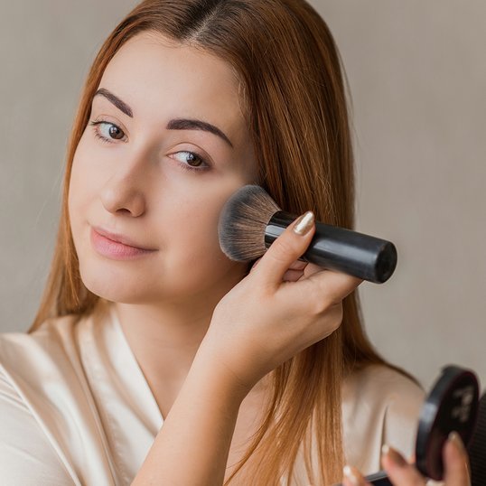 Kobieta z naturalnym makijażem aplikuje puder na twarz.